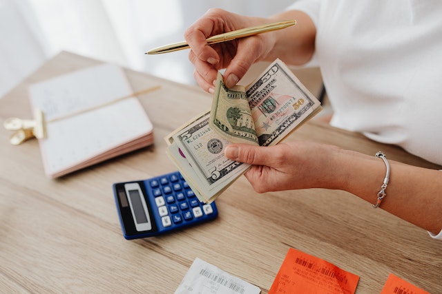 a person counting a stack of money above a calculator and notepad